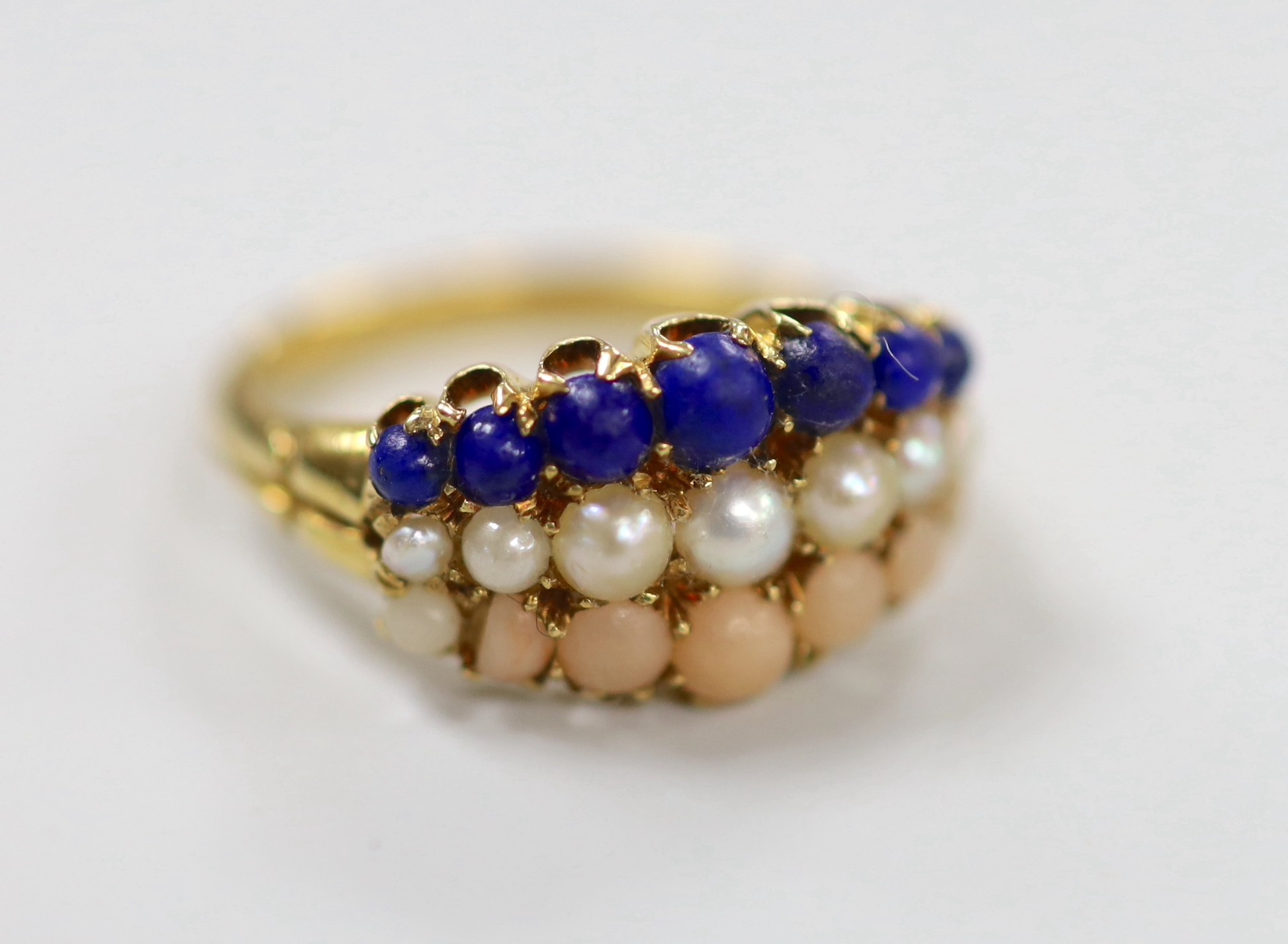 An early to mid 20th century yellow metal and graduated lapis lazuli, split pearl and coral set three row half hoop ring, size L, gross weight 4.3 grams.